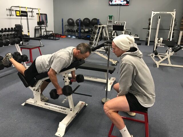 A trainer coaching a member through a dumbbell row